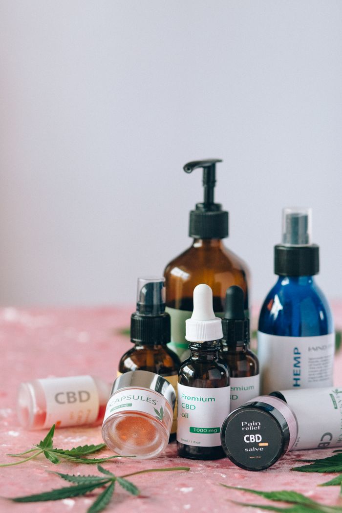 A variety of CBD products including oils and capsules on a textured pink surface with leaves.