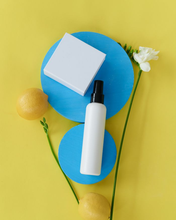 Creative flat lay of beauty products with lemons and flowers on a colorful yellow and blue background.
